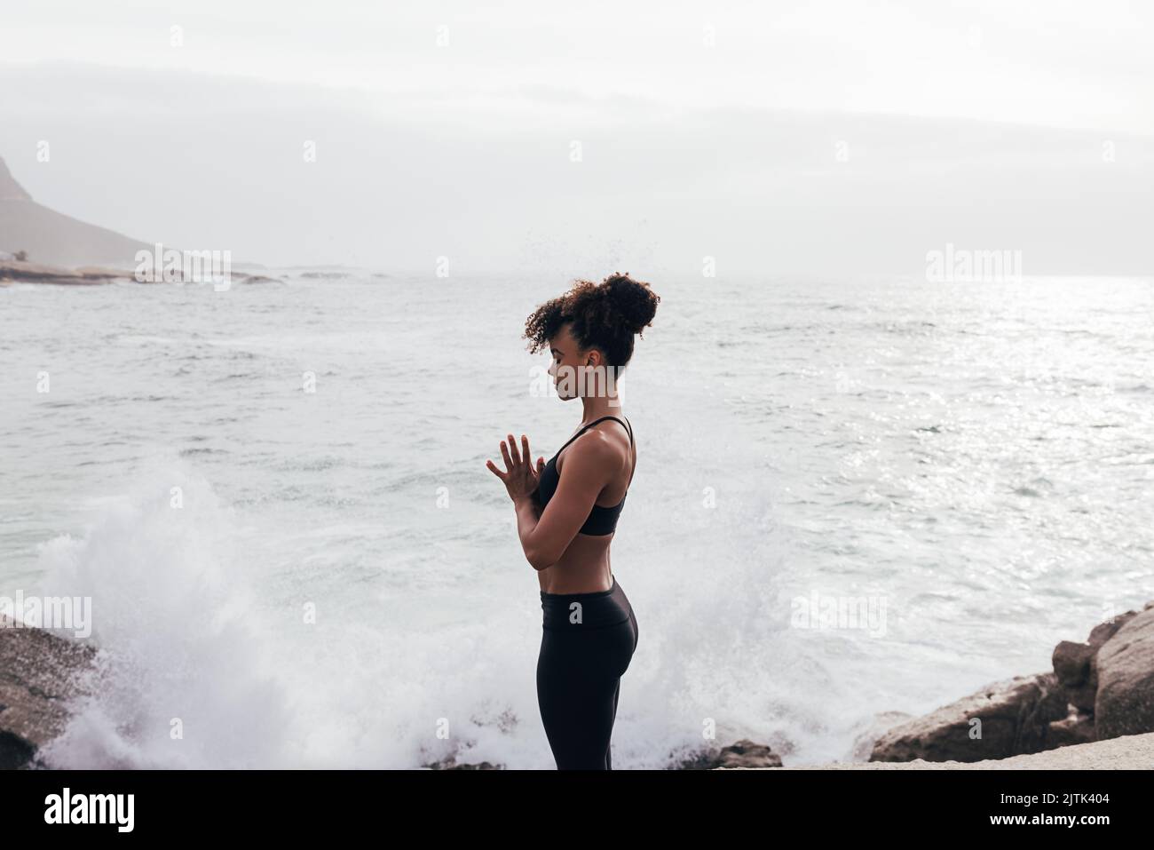 Cropped shot of young woman with folded hands meditating by ocean with closed eyes Stock Photo