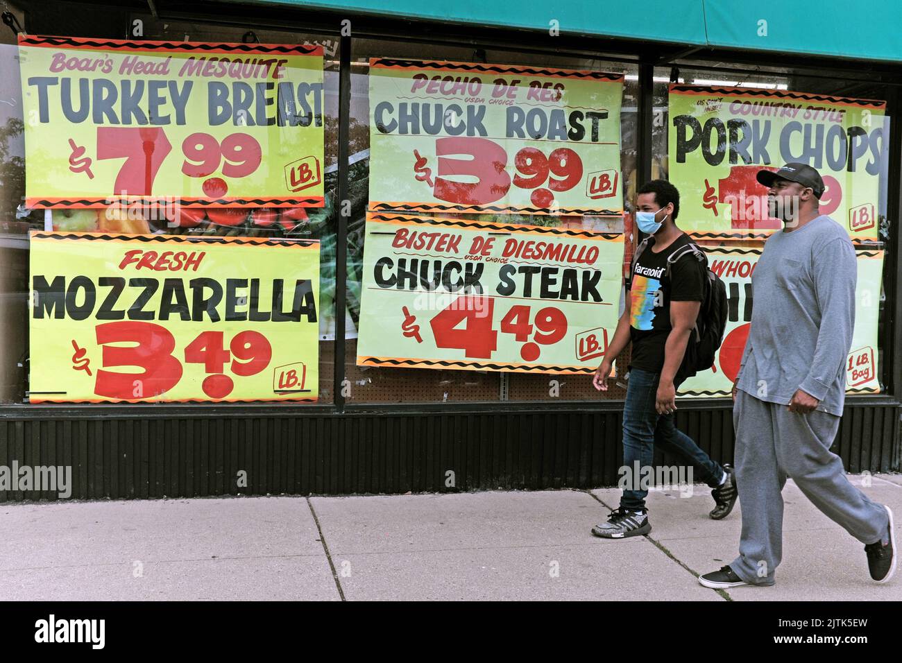 Two African-American men walk past the front windows displaying prices of food items in Edgewater Produce in Chicago, Illinois, in July 2022. Stock Photo
