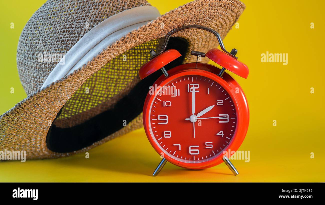 Red clock with hat on yellow background symbolizing daylight time saving Stock Photo