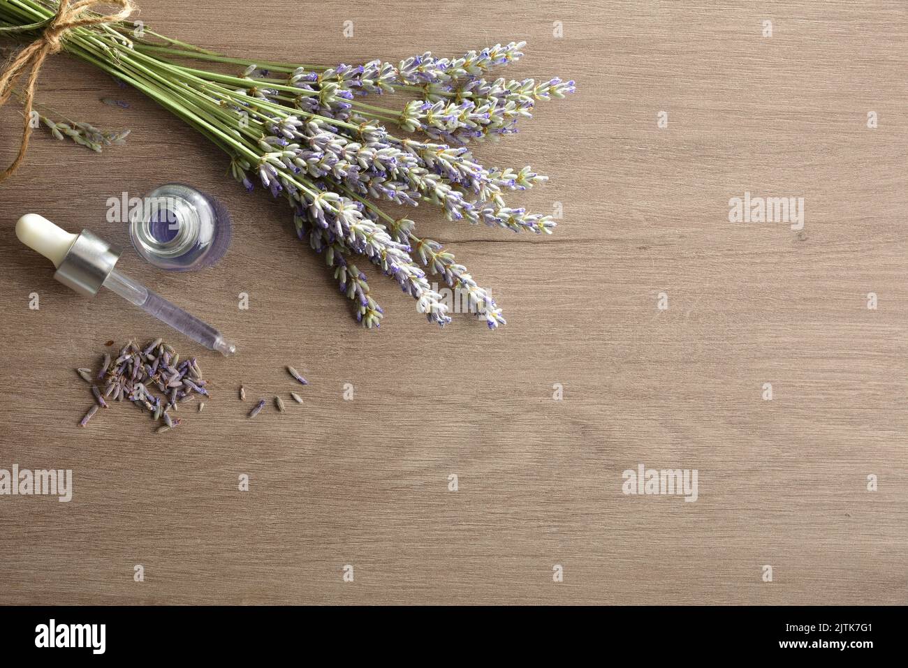 Bottle with dropper with essence of lavender on wooden table with bouquet of spikes blooming lavender. Top view. Stock Photo