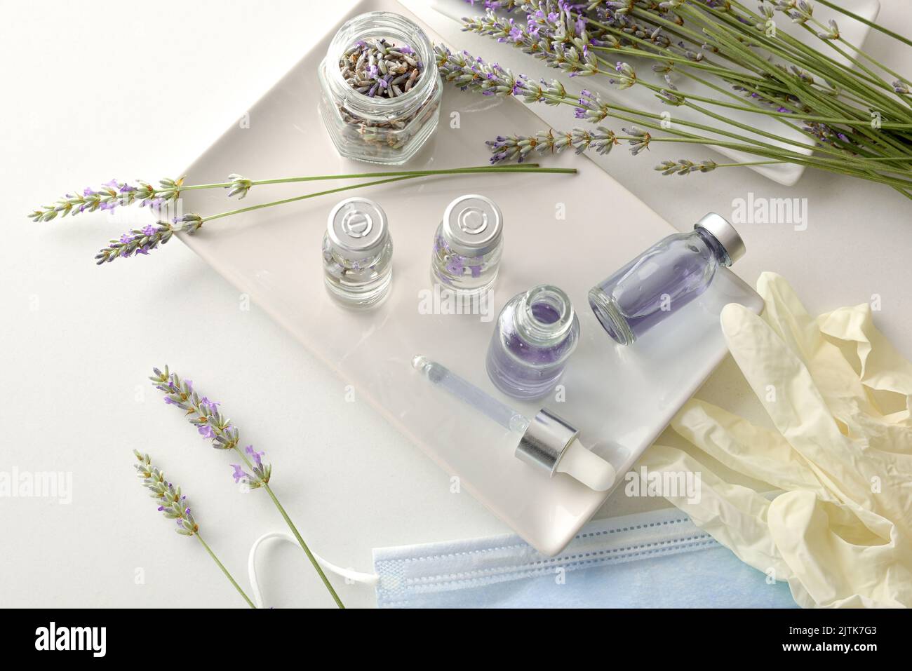 Bottles with treatment prepared from natural lavender plants on a plate on a white bench with plants and elements of protection and personal hygiene. Stock Photo