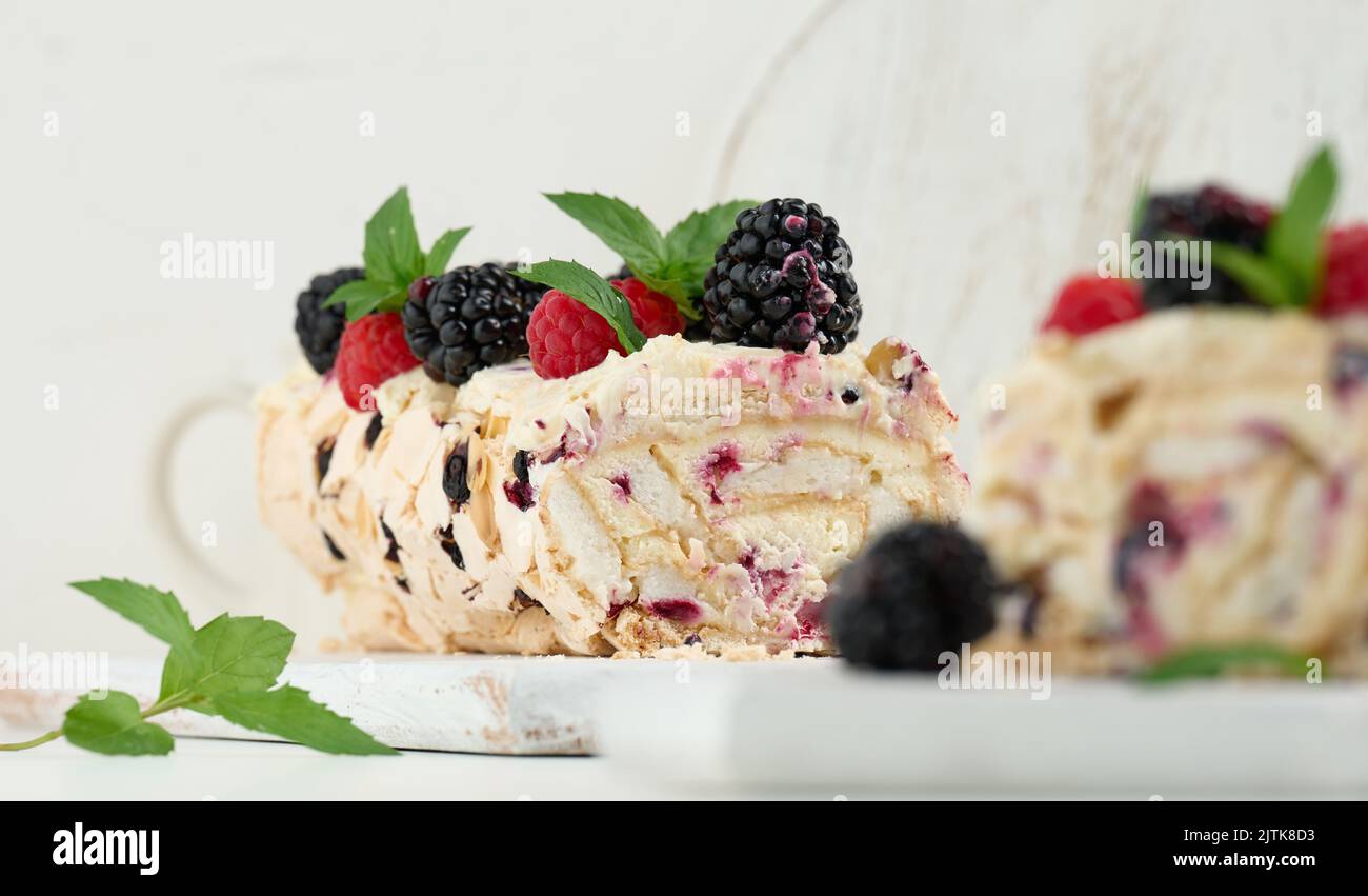 Baked meringue roll with cream and fresh fruits on a white wooden board