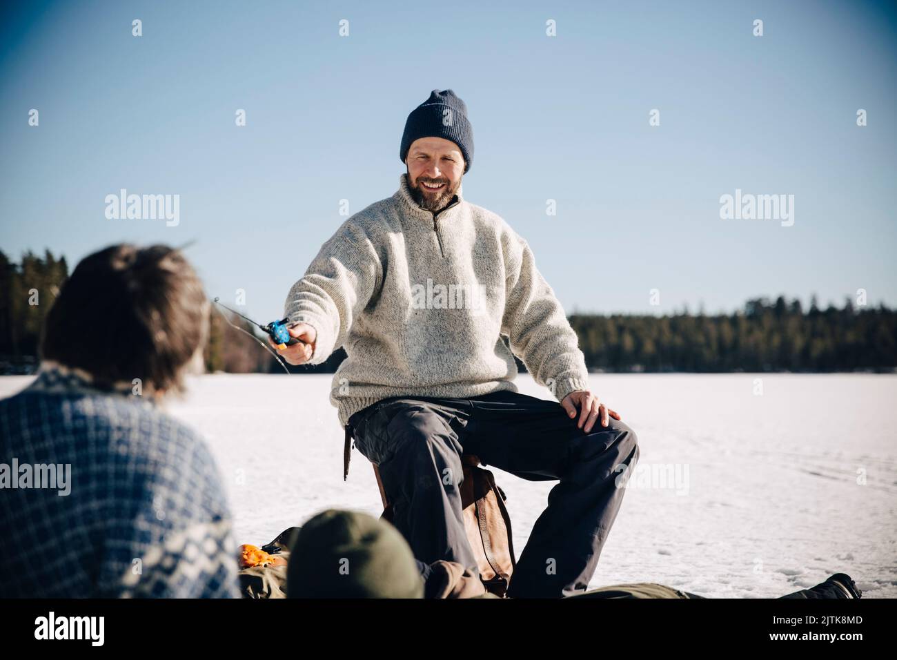 Smiling mature man giving fishing rod to friend during sunny day Stock ...