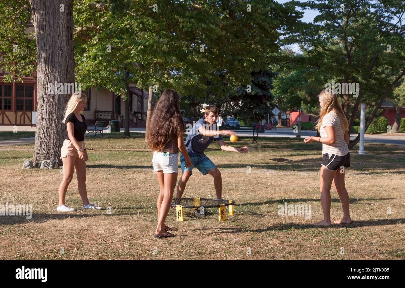 Four young mixed adults playing the Roundnet sport game of Spikeball outdoors. Stock Photo