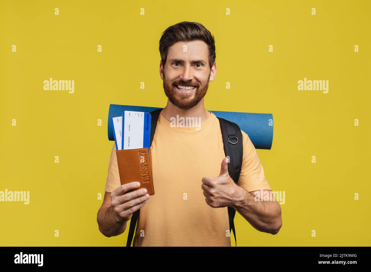 Cheap flight deals. Happy man holding tickets with passport, gesturing thumb up, standing with backpack Stock Photo