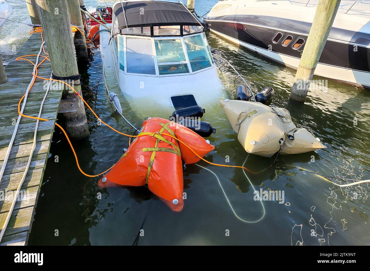 White sinking power boat being salvaged by marine airbags in a marina slip Stock Photo