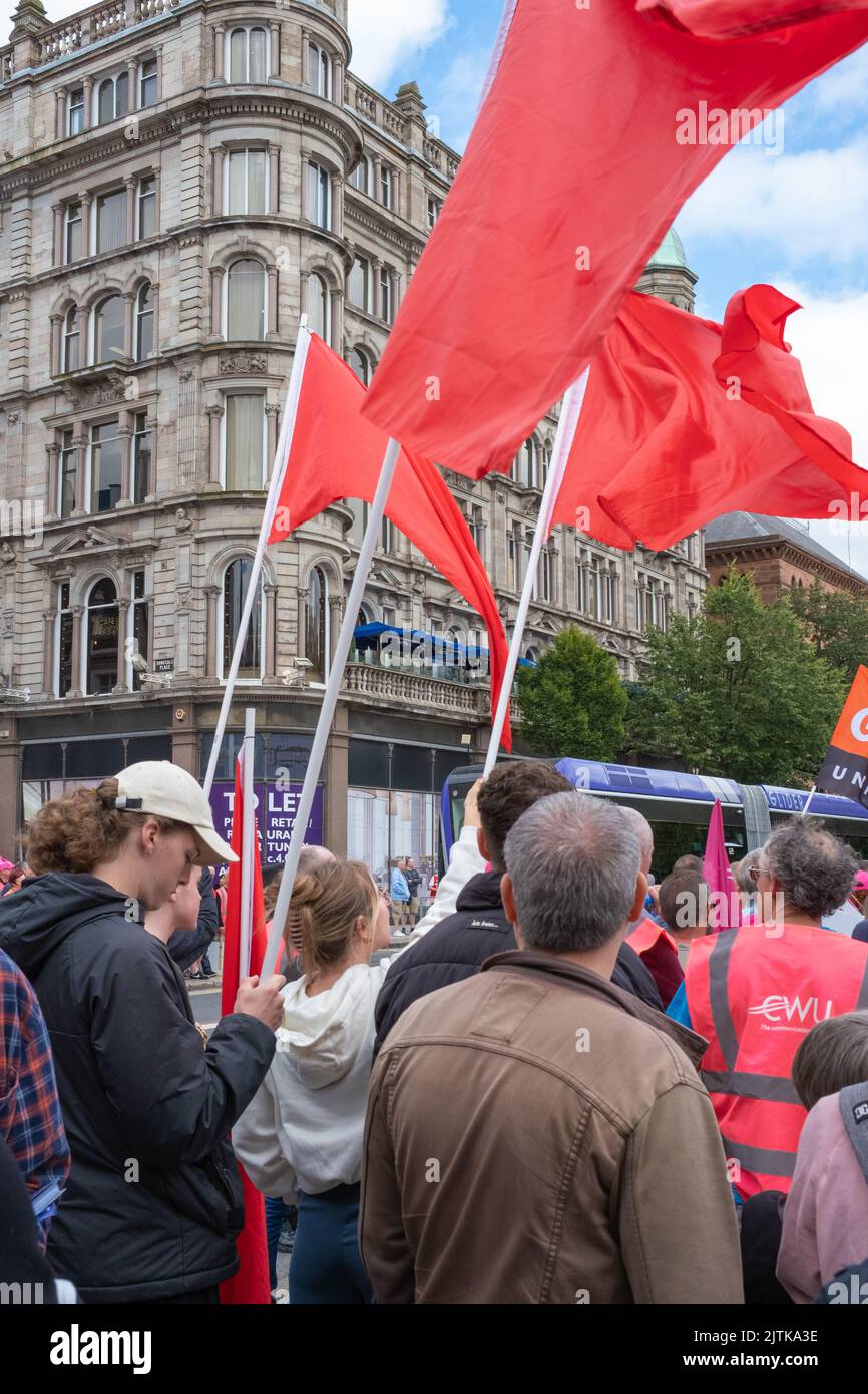 Belfast, United Kingdom. 31 Aug, 2022. Red flags waving in breeze against city centre backdrop, as campaigners gather outside Belfast City Hall to call for better pay amid rising costs of living during Communication Workers Union NI Strike Rally. Credit: Steve Nimmons/Alamy Live News Stock Photo