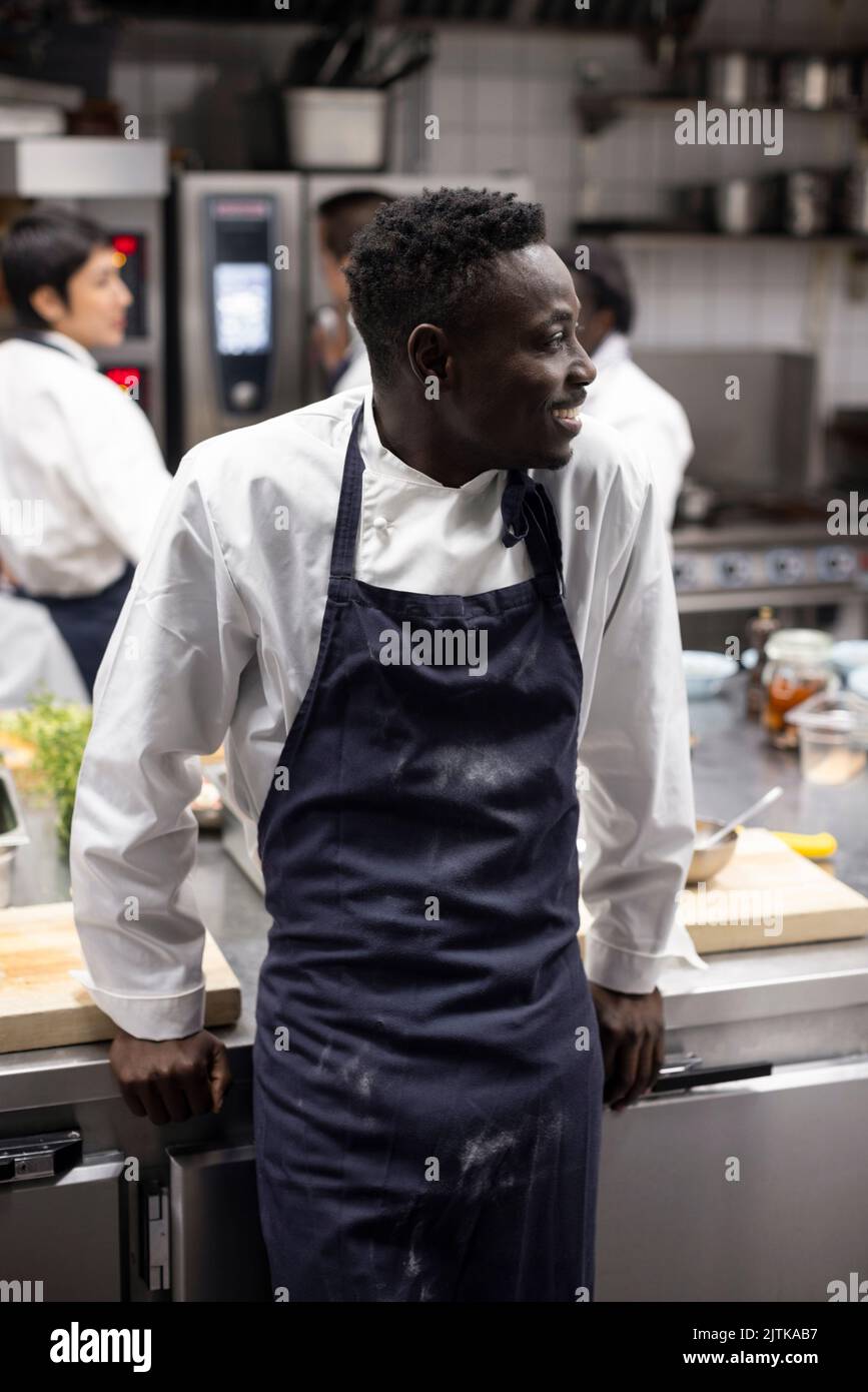 Happy man looking away while standing in commercial kitchen Stock Photo