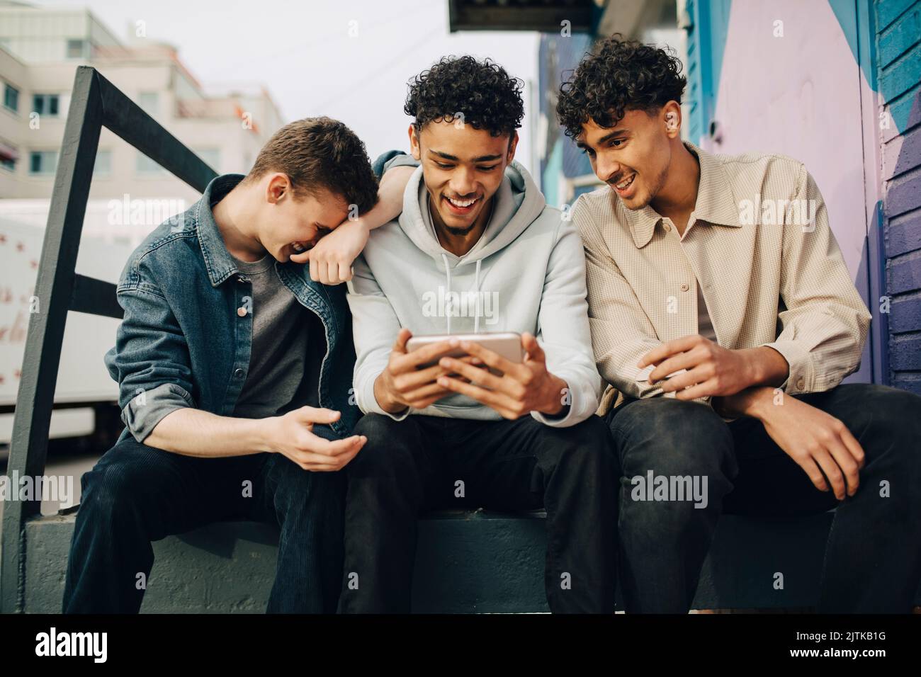 Happy man using smart phone while sitting with friends outdoors Stock Photo