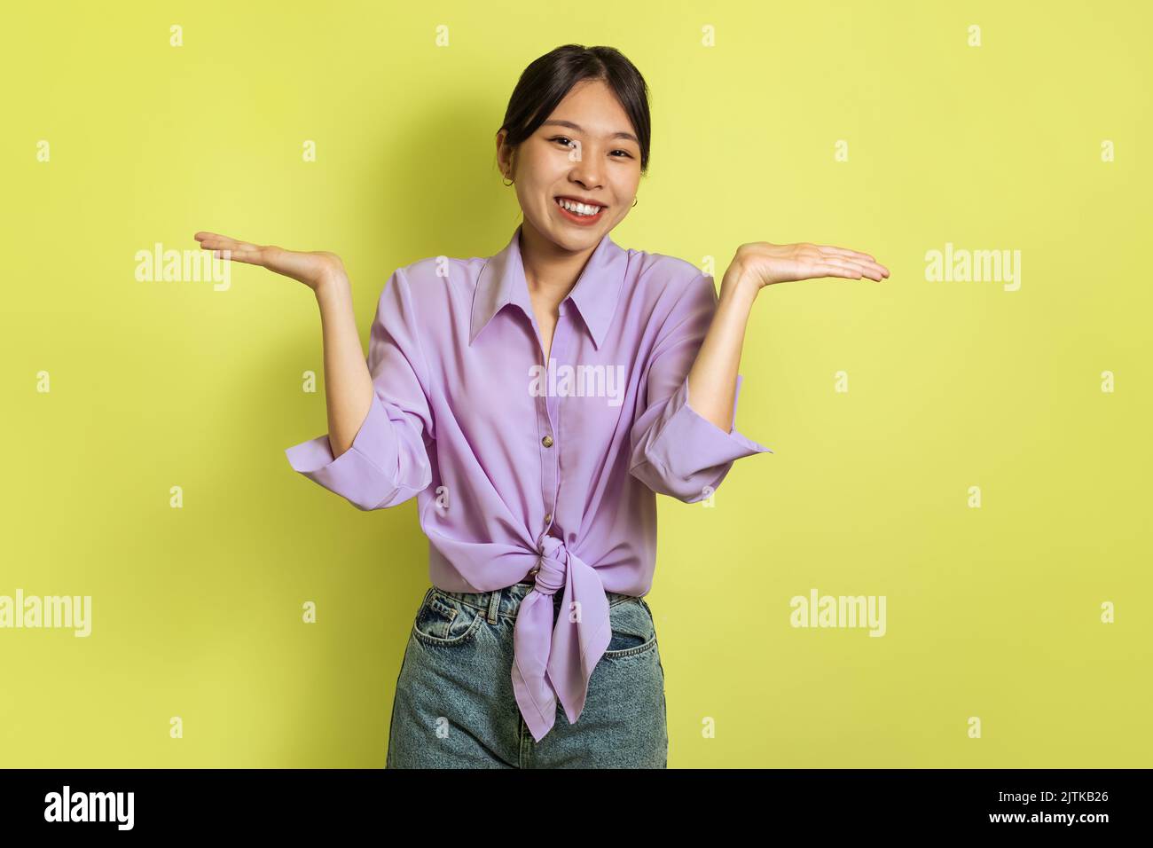 Asian Lady Shrugging Shoulders Smiling To Camera Over Yellow Background Stock Photo