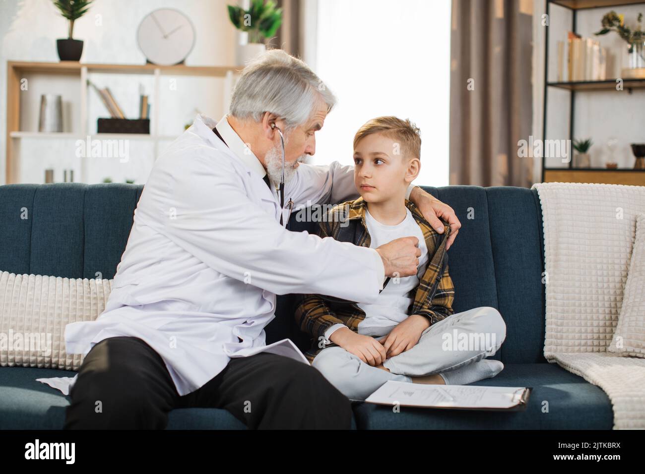Preschool sick cute boy sitting on the couch while caring experienced nice mature male doctor listening his heartbeat during home visit front view Stock Photo Alamy