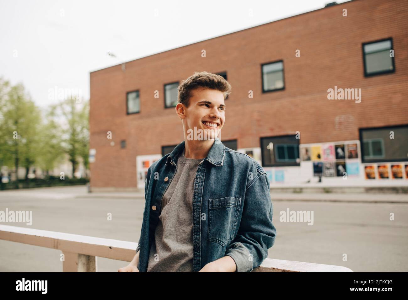 Smiling young man looking away while leaning on railing Stock Photo