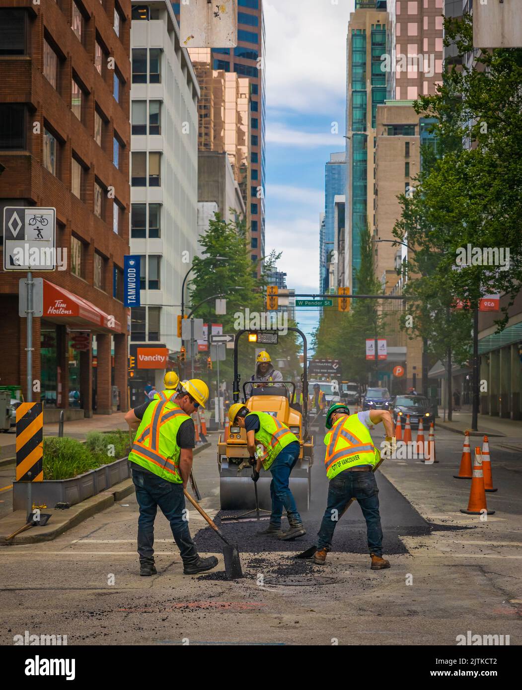 Team of workers put the hot asphalt on a road. Road construction workers with shovels in protective uniforms. Road Construction Works in a city-July 1 Stock Photo