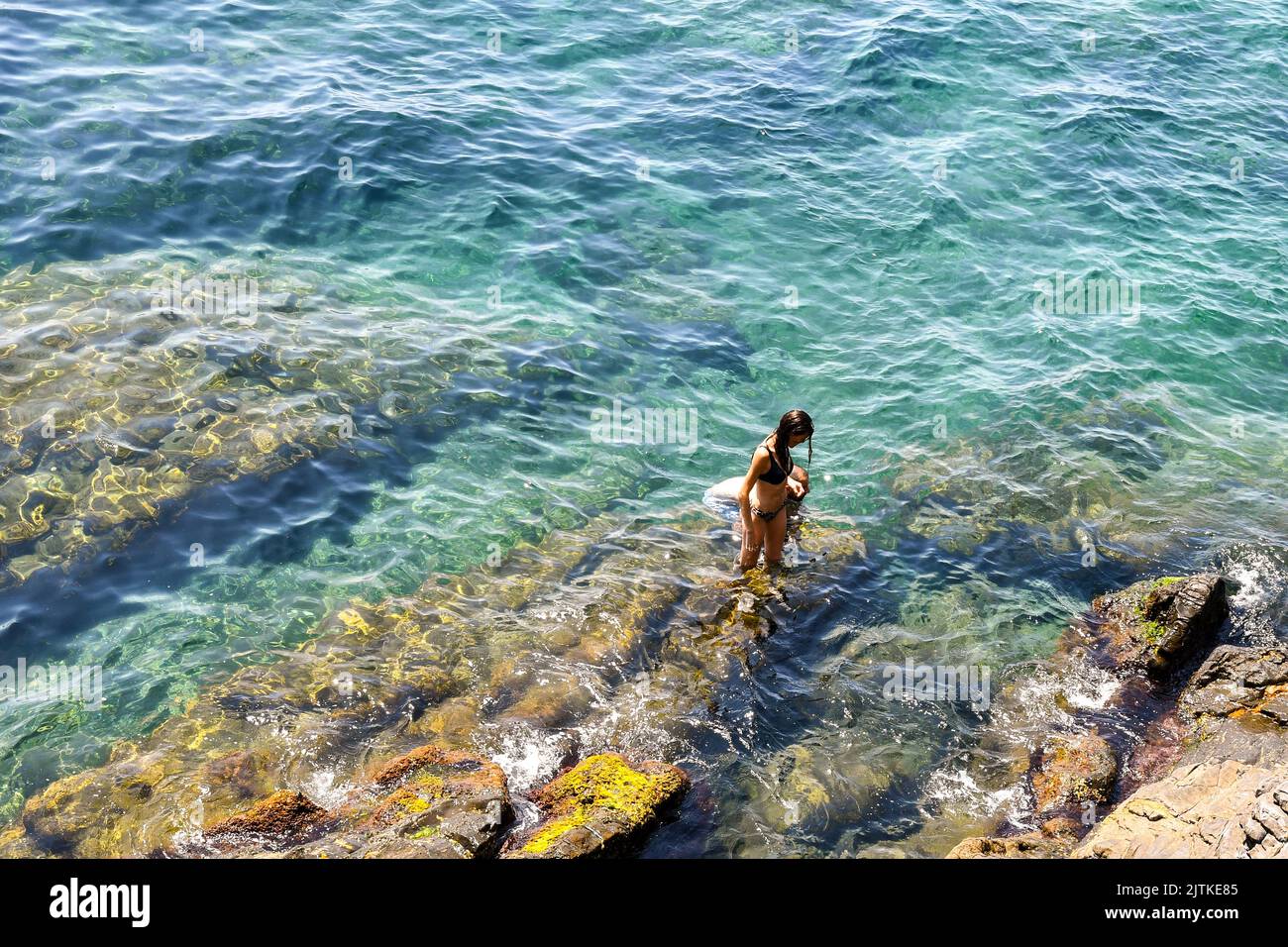A young woman standing on the rocks of the seashore in summer, Nervi, Genoa, Liguria, Italy Stock Photo