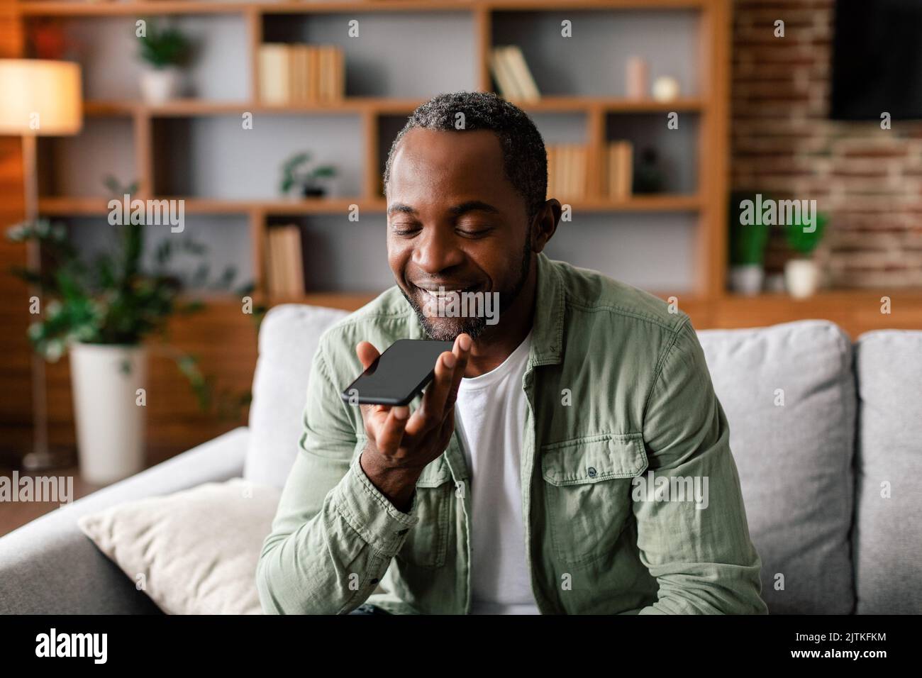 Cheerful middle aged african american male calling by smartphone with blank screen in living room interior Stock Photo