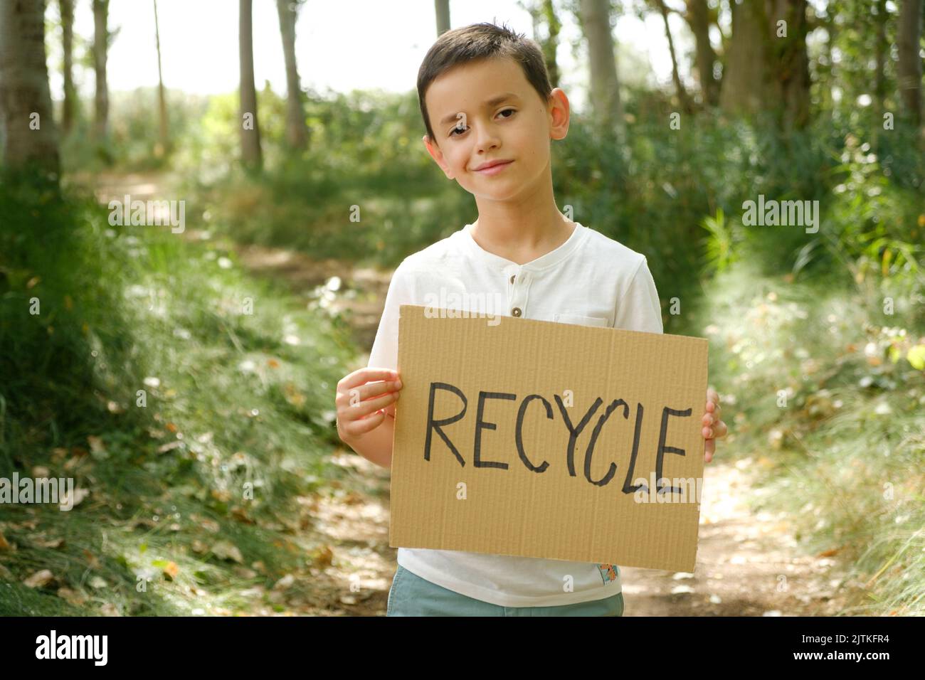child in the forest displays sign with the message 'recycle' Stock Photo