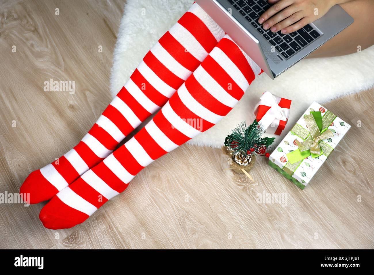 Girl in Christmas knee socks sitting on a fur rug with laptop near the gift boxes. Ordering gifts, work and leisure at home during New Year holidays Stock Photo