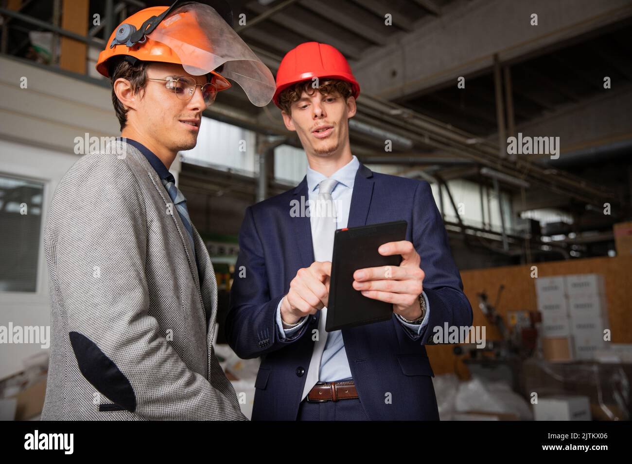 Two engineers discuss a project using a tablet while they are in the factory Stock Photo