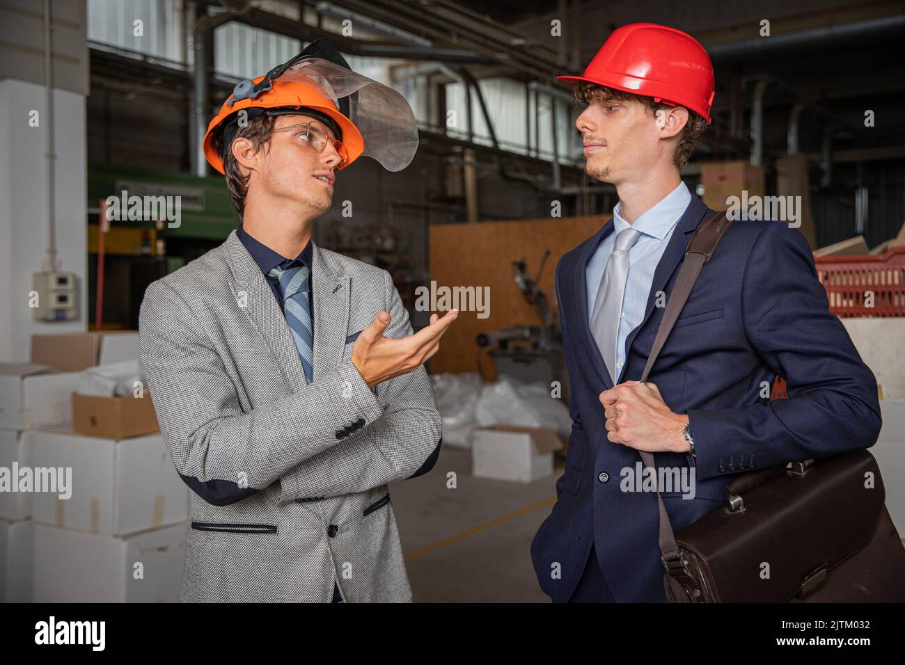Two colleagues during a conversation at work in the factory, engineers elegantly dressed wear protective helmet Stock Photo