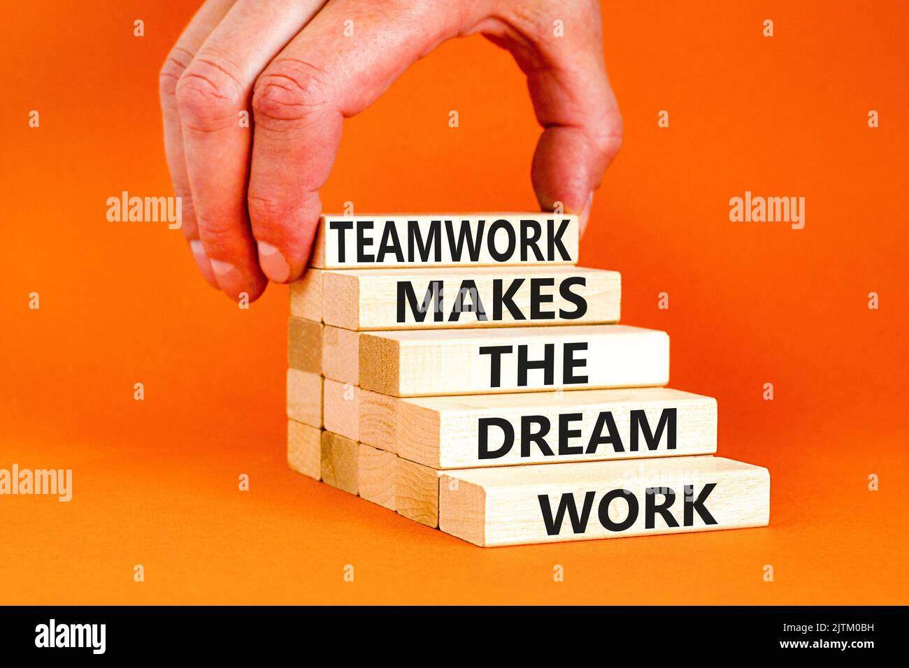 Teamwork makes dream work symbol. Concept words Teamwork makes the dream work on wooden blocks on beautiful orange background. Businessman hand. Busin Stock Photo