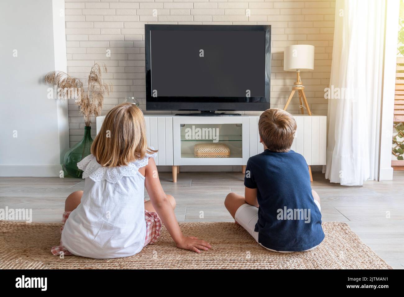 Two children sitting on the living room floor watching television. Mock up for inserting images in the tv Stock Photo