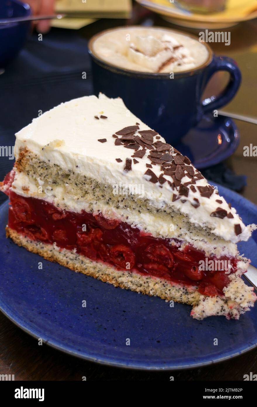 Slice of cherry layer cake with cream and a cup of cappuccino Stock Photo