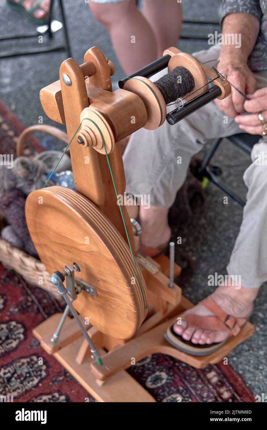 A woman spins wool yarn on a modern, wooden, dual treadle spinning wheel at the National Folk Festival Folk Life area in Salisbury, Maryland. Stock Photo