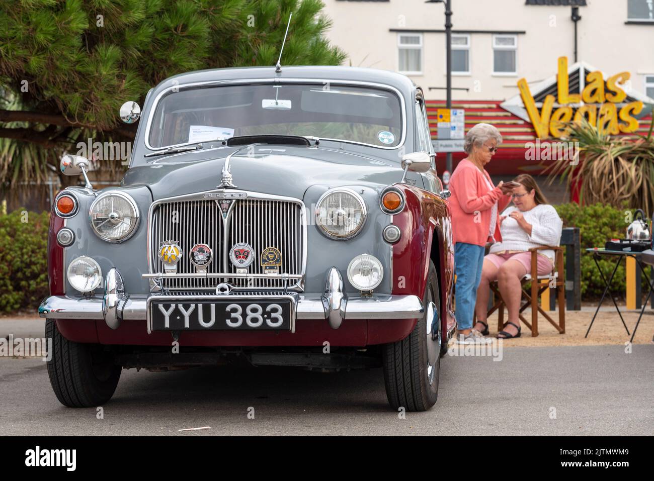 1960 Rover 100 saloon car on show on Marine Parade, Southend on Sea, Essex, UK. Women, possibly partners of owners, passing the time nearby. Camp seat Stock Photo