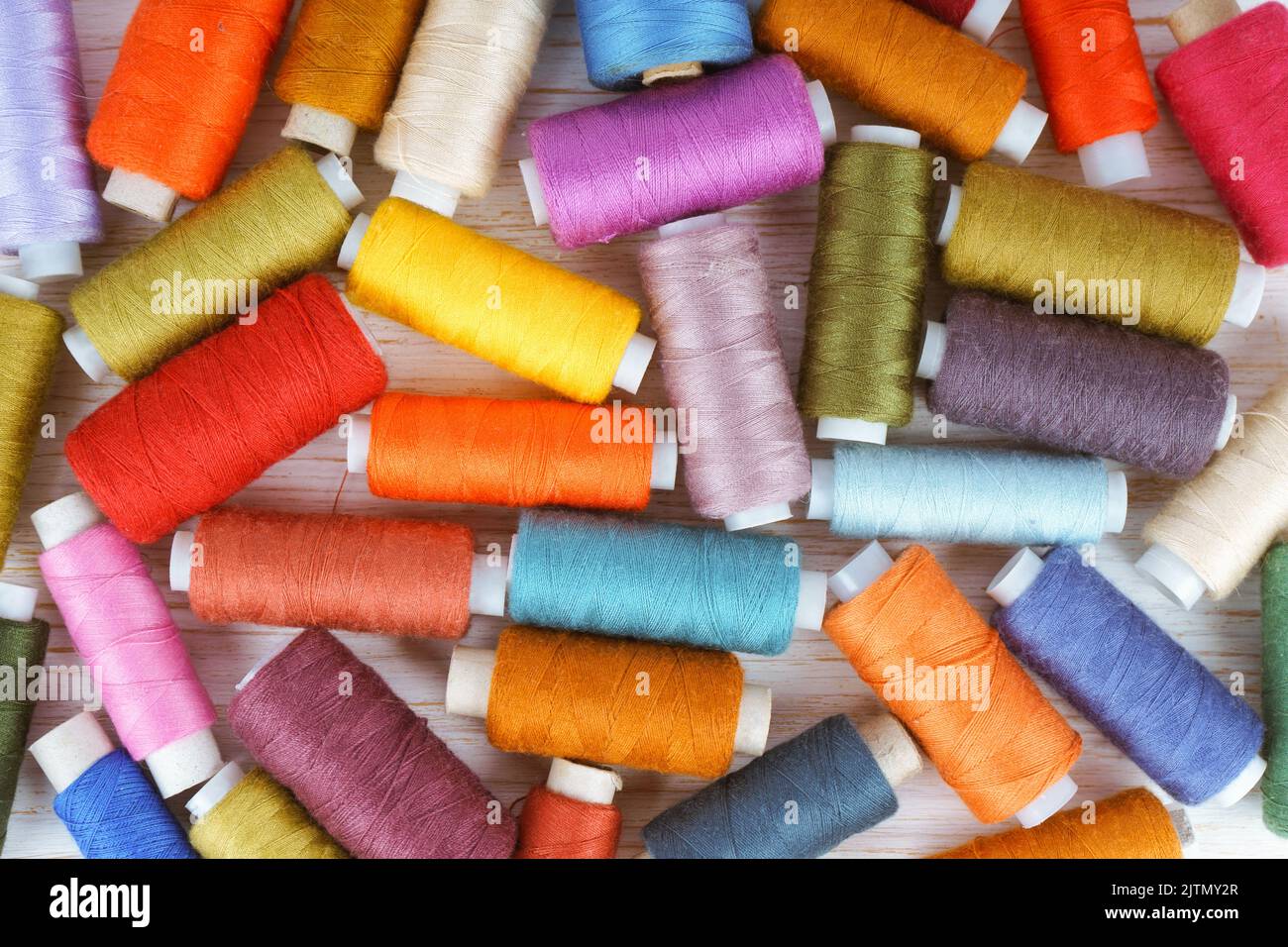 Scattering of various colors sewing threads on white wooden background. Flat lay, top view. Stock Photo