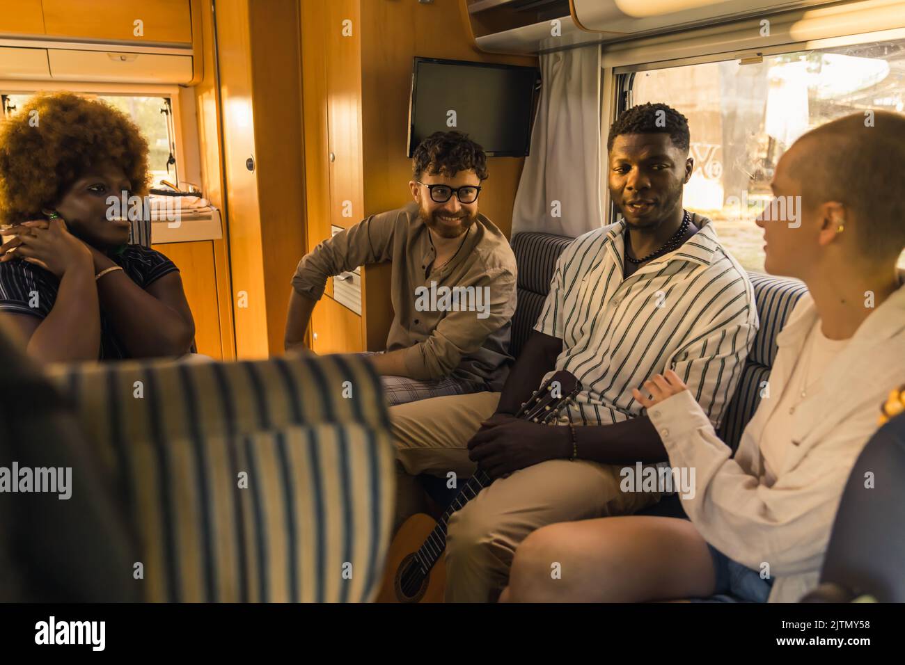 Interracial group of four good friends on a summer road traveling, sitting inside their comfortable modern motorhome, chatting and relaxing. RVs interior. High quality photo Stock Photo