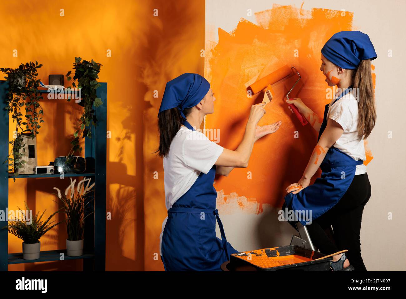 Mom and child using tools to paint walls with orange color, renovating apartment interior with