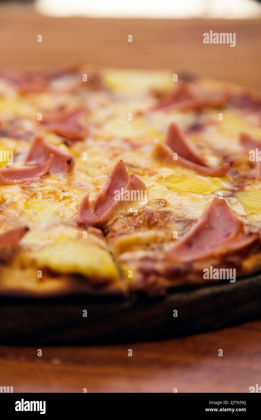Hawaiian pizza with cheese, ham and pineapple, served on a wooden board in an Italian restaurant. Stock Photo