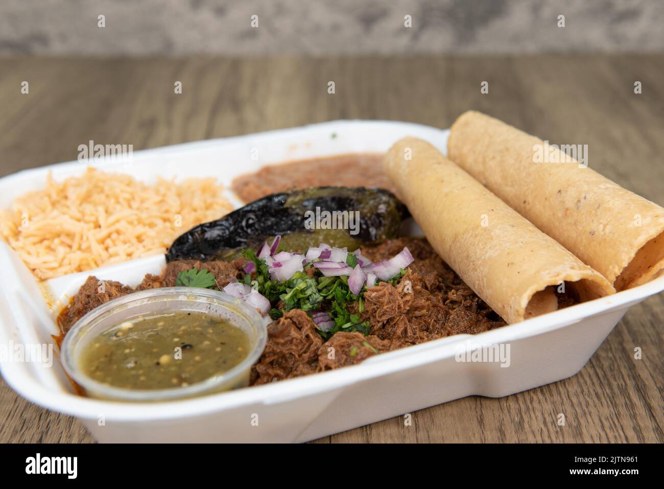 Generous serving of slow cooked birria meat, served with corn tortillas, rice, beans, and salsa for a tempting meal. Stock Photo