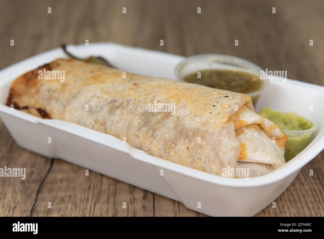 Loaded mexican cuisine burrito, bulging at the flour tortilla and served with a grilled jalapeno, salsa, and guacamole. Stock Photo