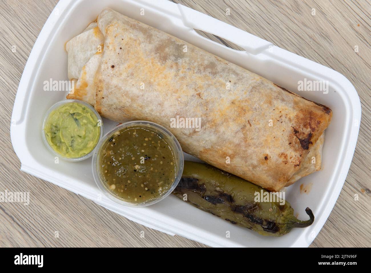 Overhead view of loaded mexican cuisine burrito, bulging at the flour tortilla and served with a grilled jalapeno, salsa, and guacamole. Stock Photo