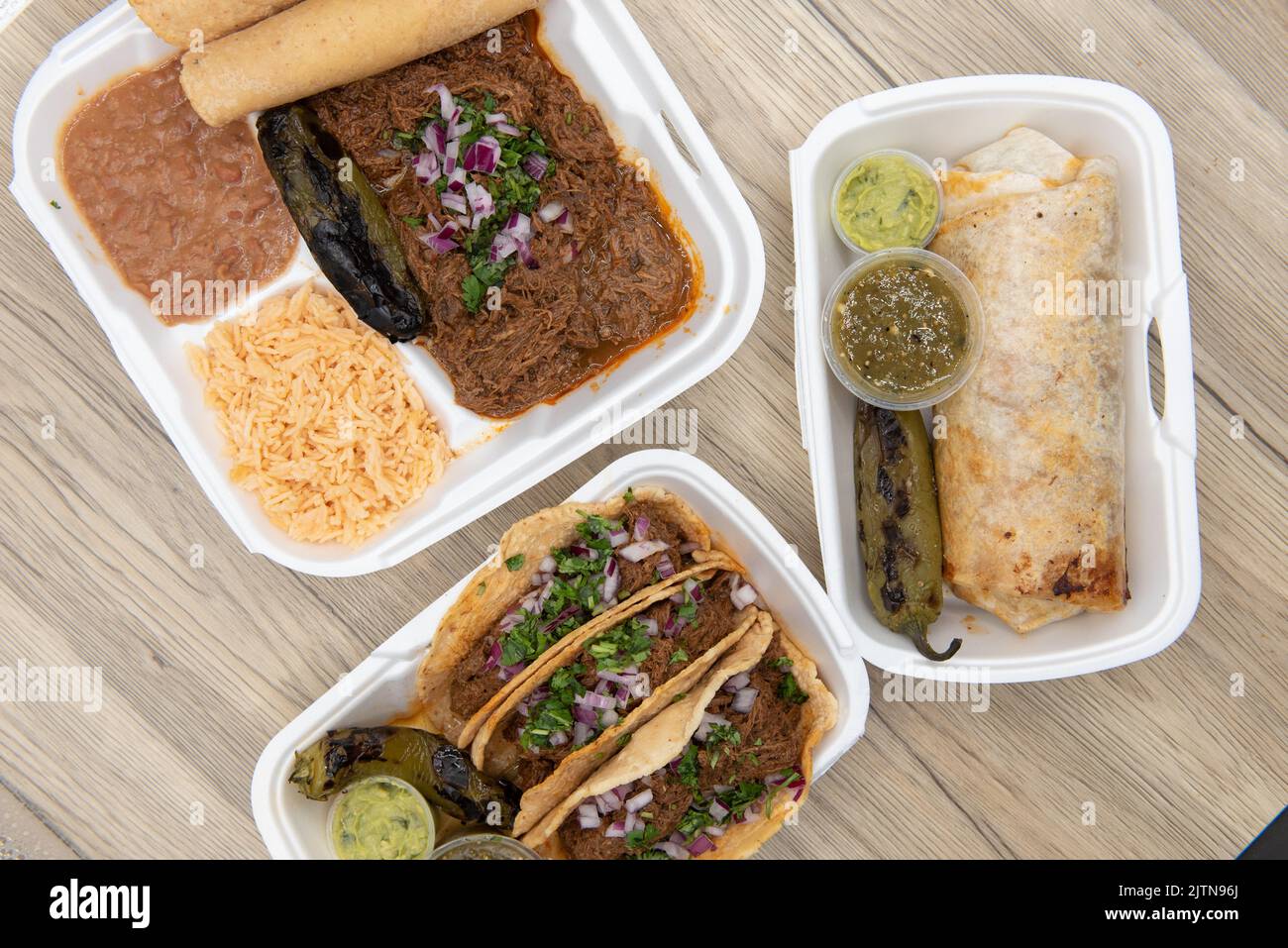 Overhead view of Mexican food feast on the table with choices of burrito, birria stew meat combo, or 3 tacos served with guacamole, salsa, and a grill Stock Photo
