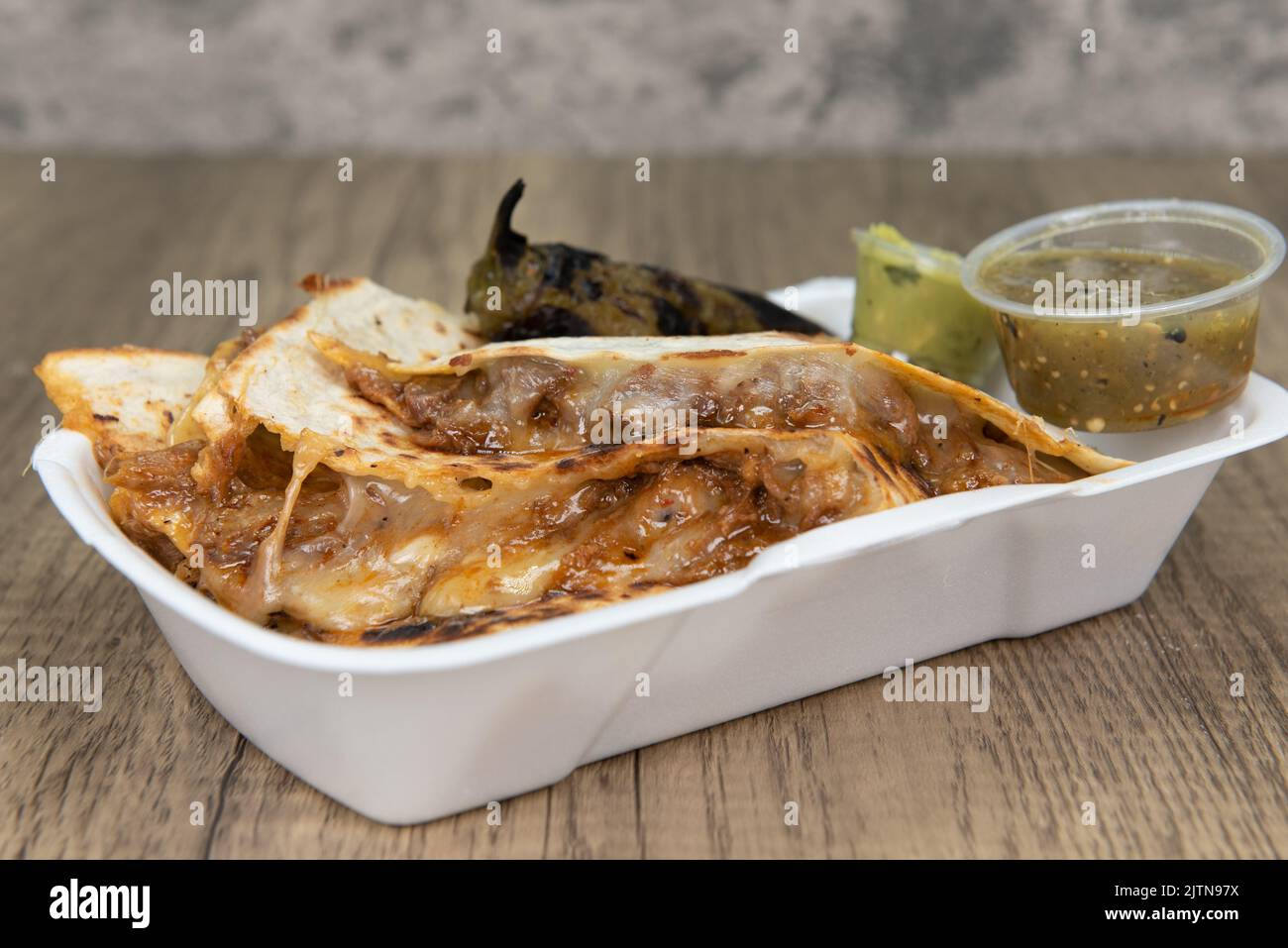 Grilled birria quesadillas are oozing melted cheese out from between the tortillas and served with grilled jalapeno, salsa, and guacamole. Stock Photo