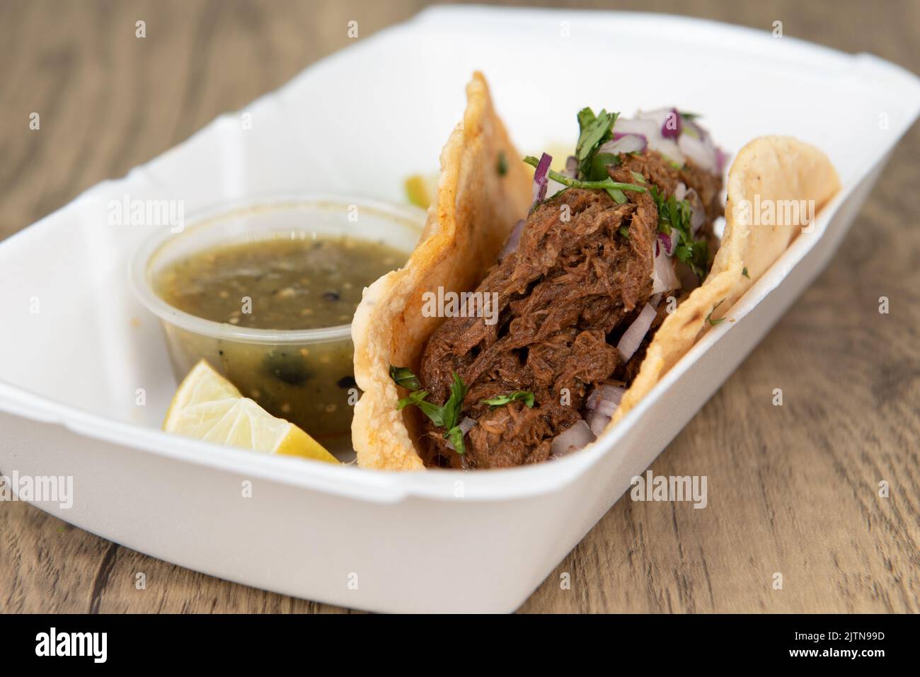 Single birria taco completely fills the tortilla shell and served with salsa and limes as an appetizer. Stock Photo