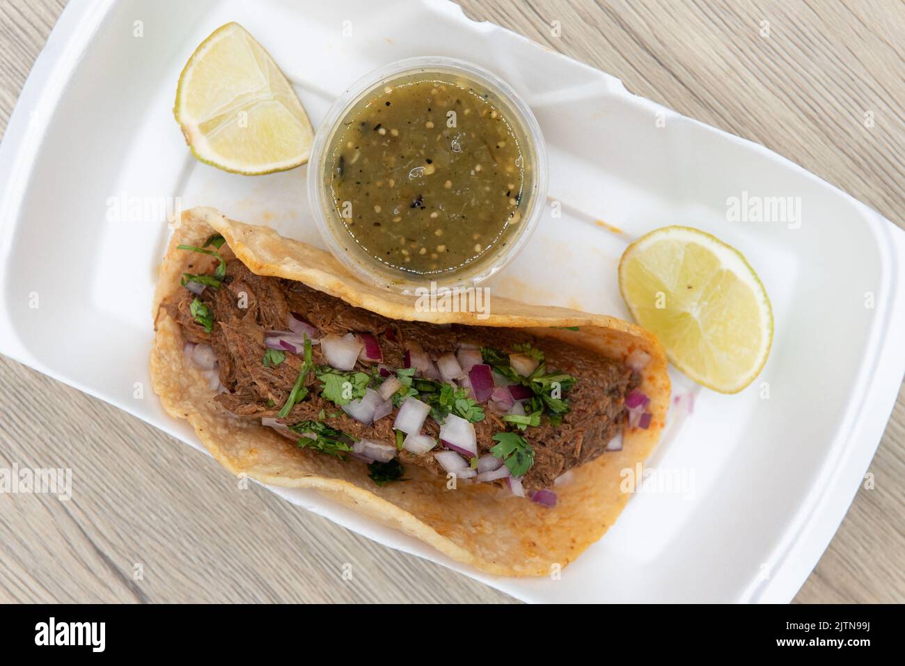 Overhead view of single birria taco completely fills the tortilla shell and served with salsa and limes as an appetizer. Stock Photo