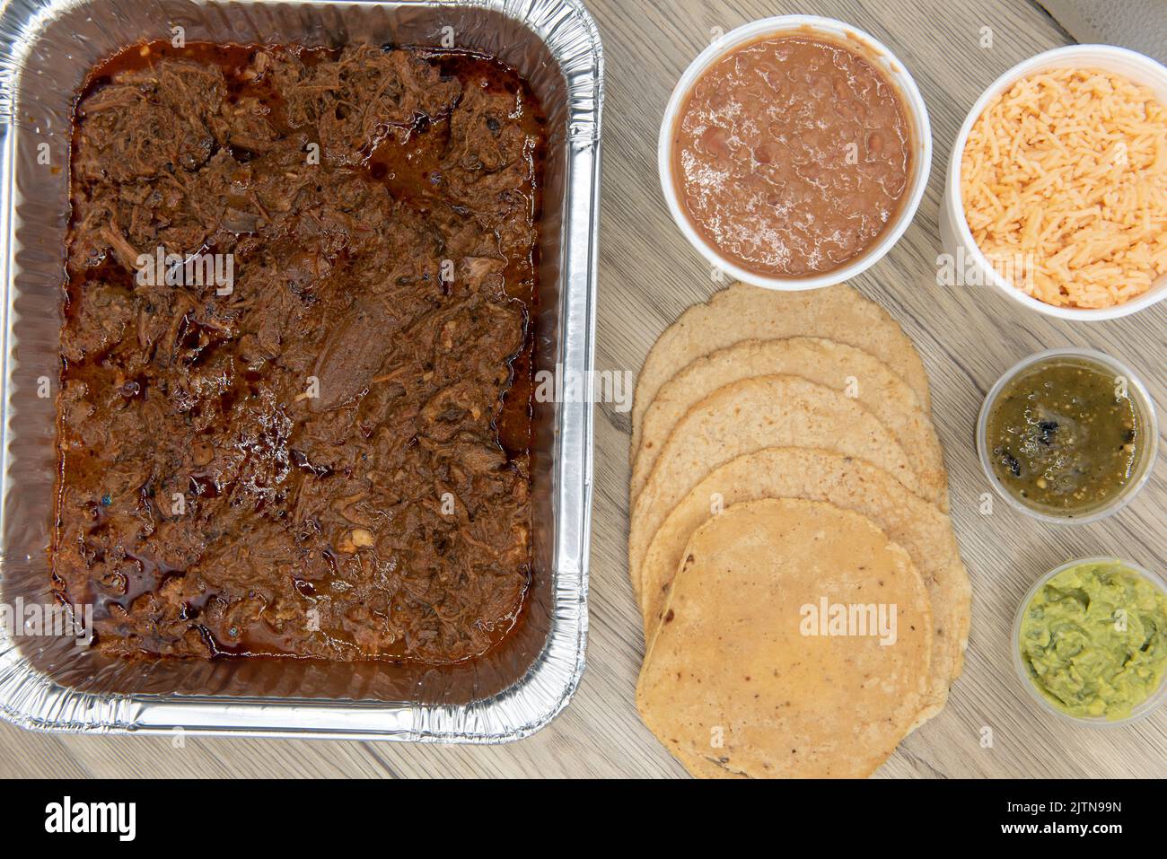 Overhead view of family sized Mexican food meal comes with slow cooked birria, homemade tortillas, rice, beans, salsa, and limes to feed everyone. Stock Photo