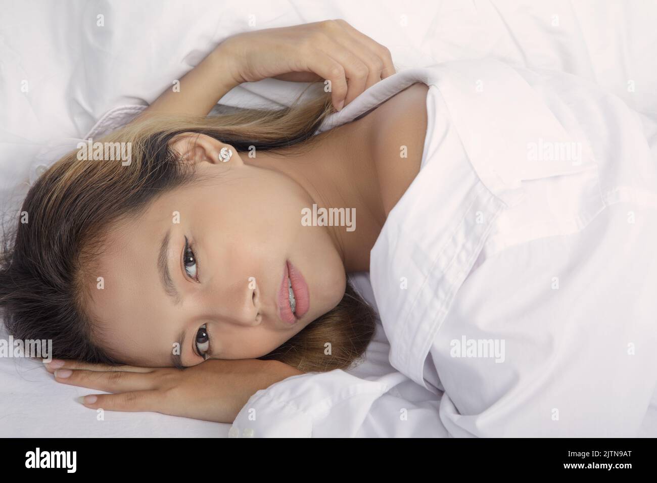 Beautiful Asian woman posing nude on a bed wearing a white shirt with white sheets Stock Photo