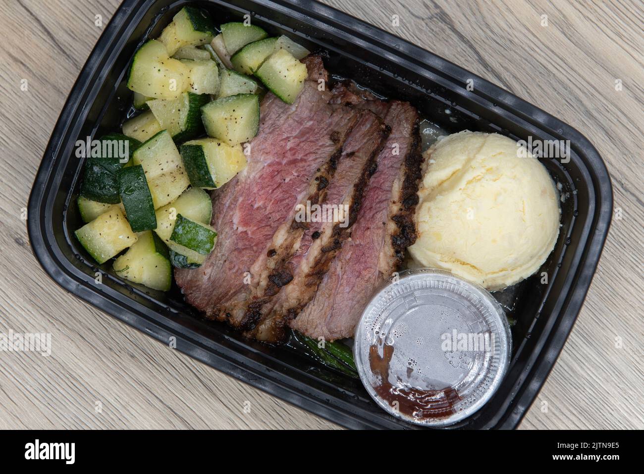 Overhead view of take out order of Tri tip steak with mashed potatoes is conveniently packed in a microwavable container. Stock Photo