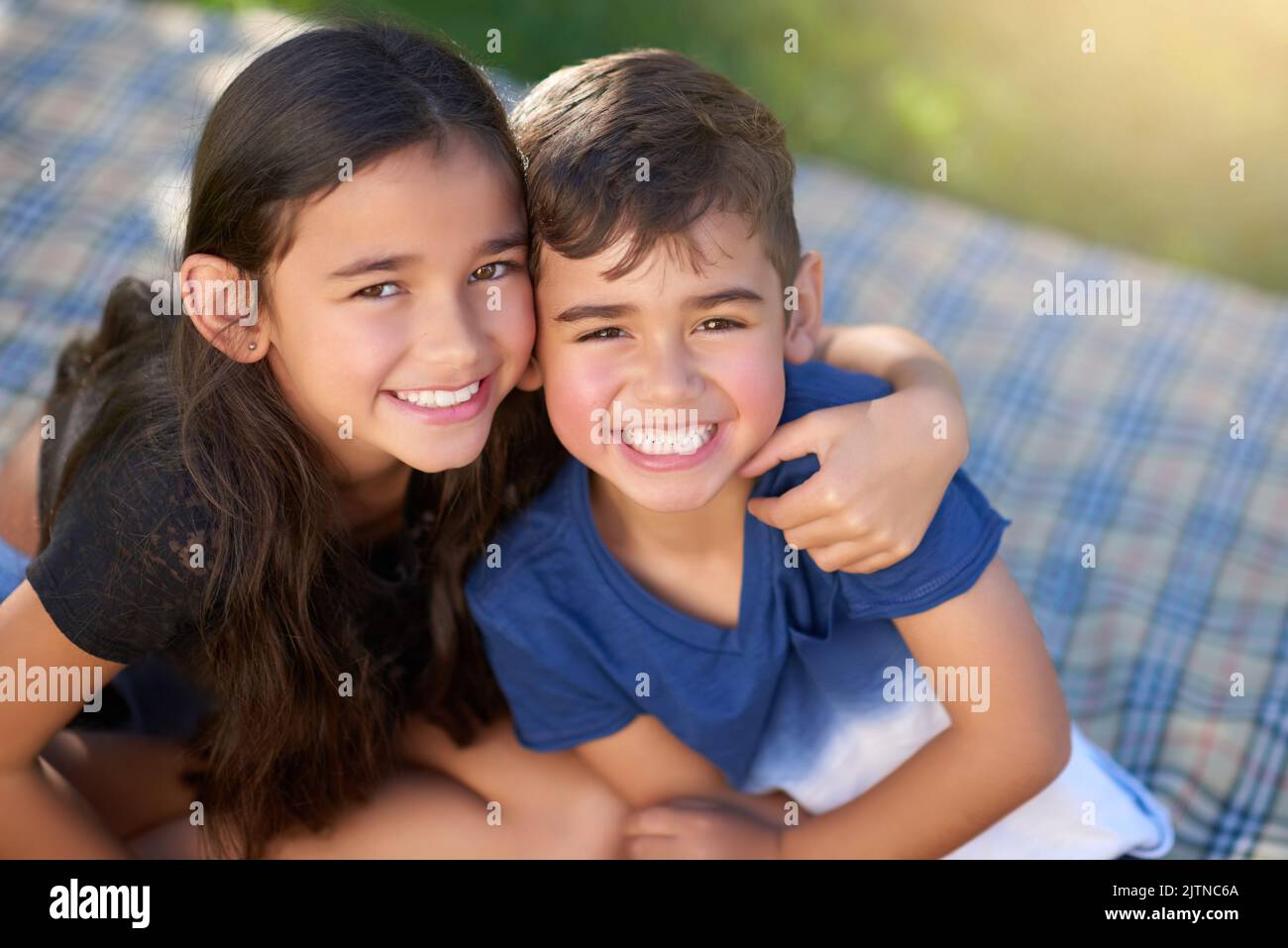 Sibling rivalry Whats that. Portrait of a pair of young siblings hugging each other while sitting in their backyard. Stock Photo