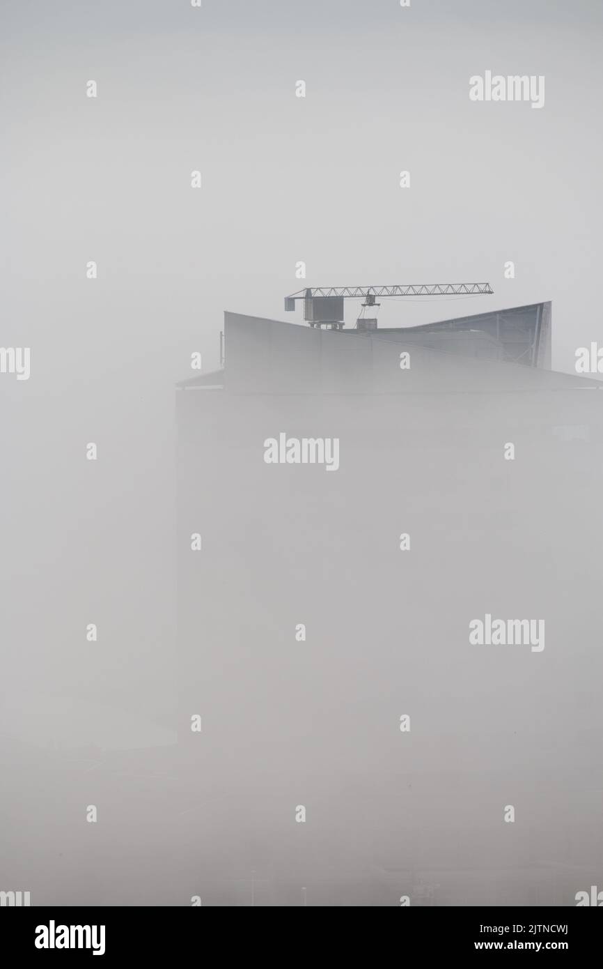 Top of skyscraper with crane appears through fog Stock Photo