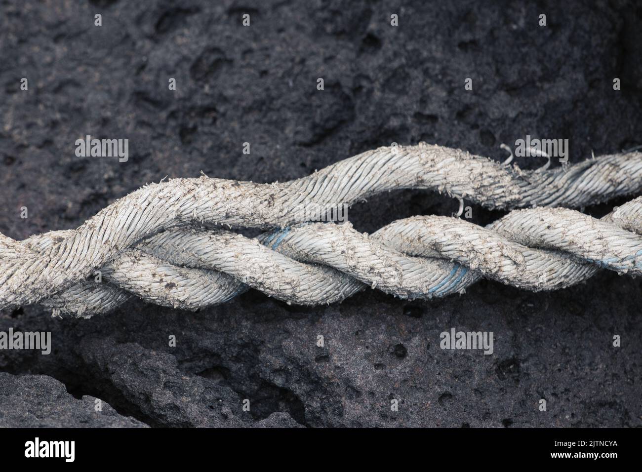 Old white rope on black rock unravels Stock Photo