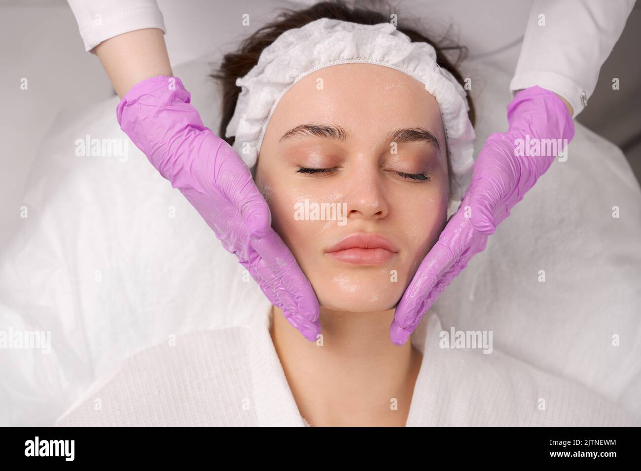 Facial massage beauty treatment. Close-up of a young woman face lying on back, getting face lifting massage, Stock Photo