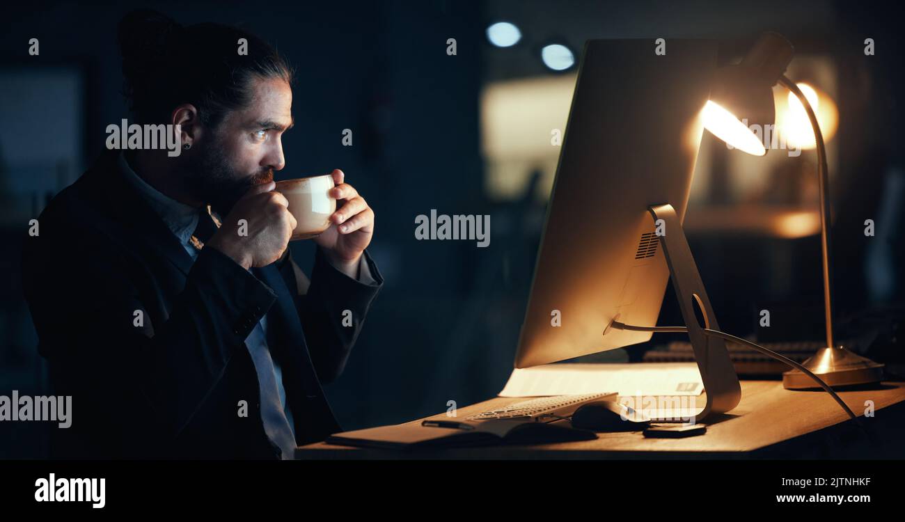 Coffee, night and commitment with a business man working late in a dark office on a deadline. Male corporate professional at work on a computer at his Stock Photo
