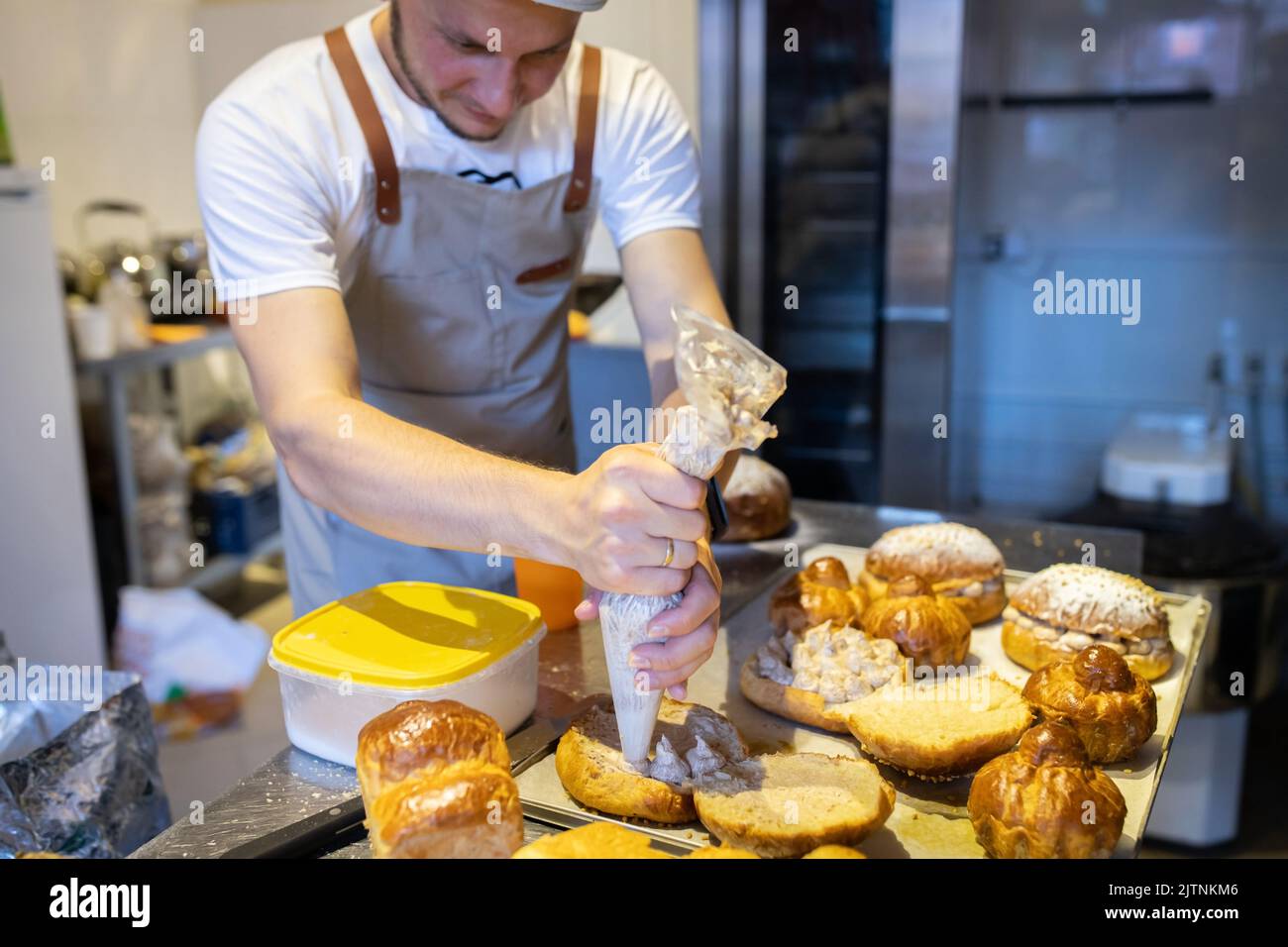 A male baker in a small artisan bakery fills brioches with cream. Front