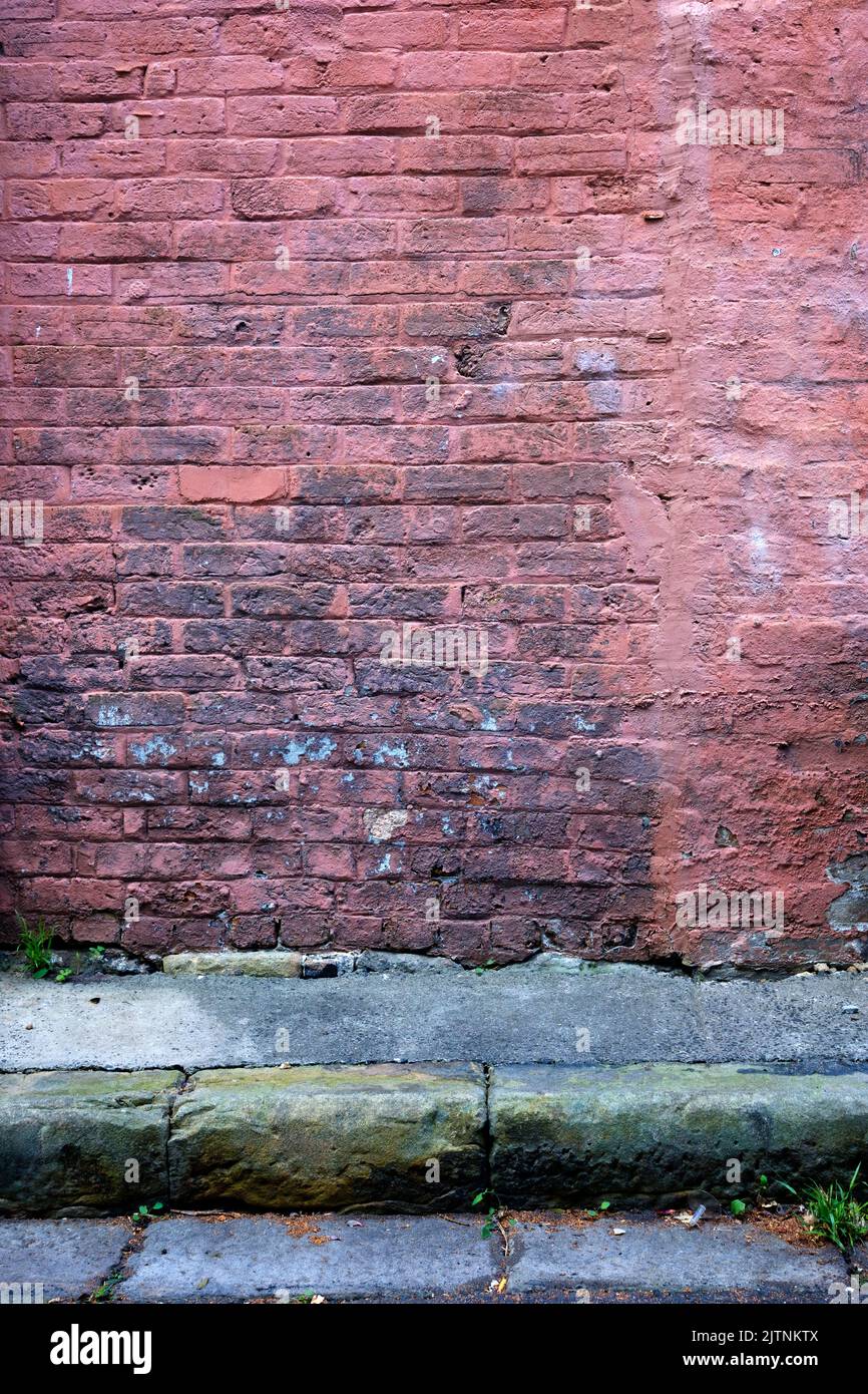 An old brick wall with faded paint with road and rain water gutter in