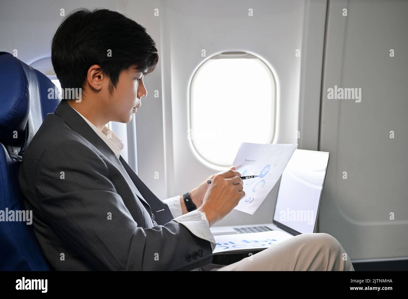 Professional Asian businessman concentrating reading and analyzing a financial data report during on the flight to his business trip. Stock Photo